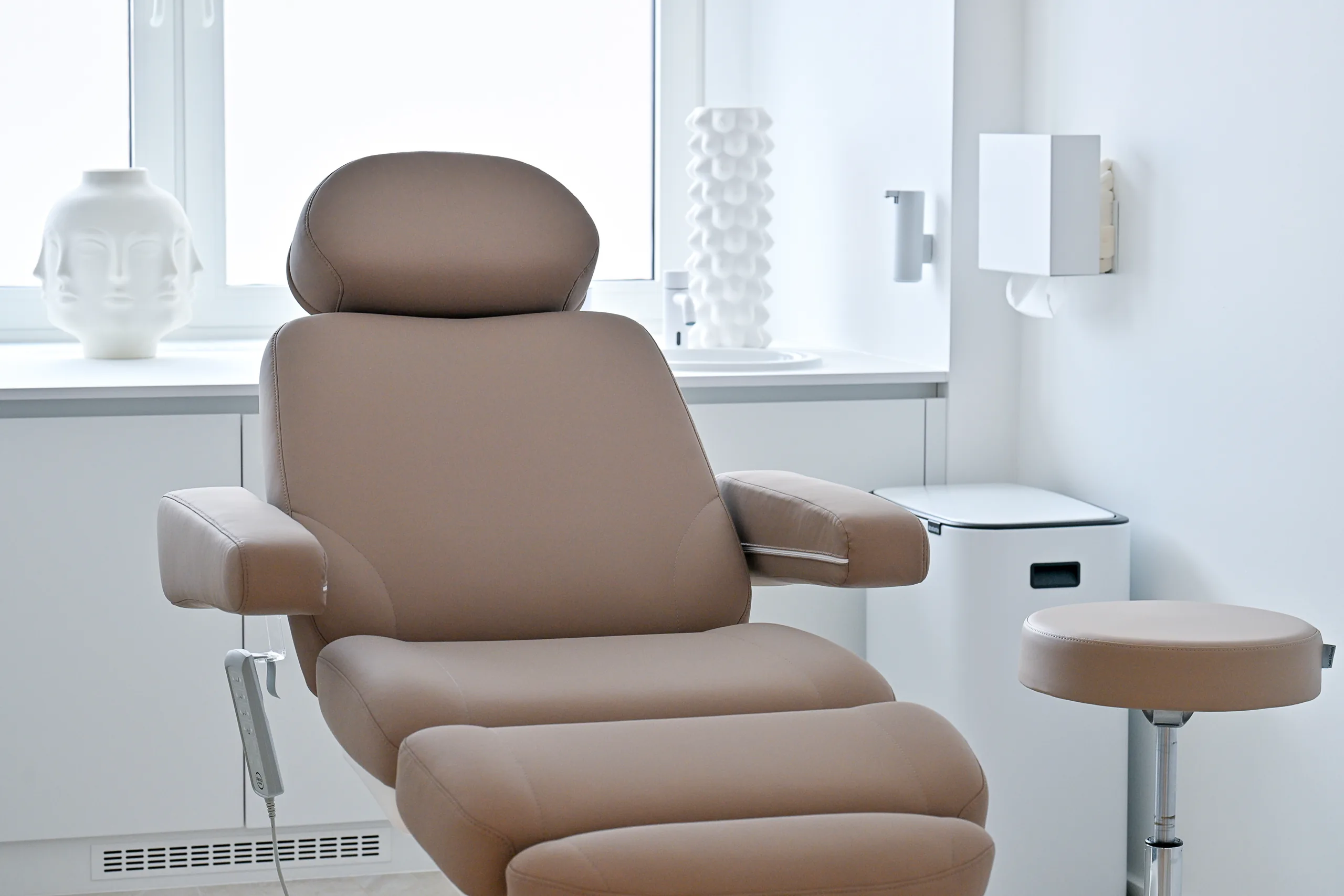 Beige treatment couch with a stool by the window of a bright treatment room at the artethic® practice in Düsseldorf.