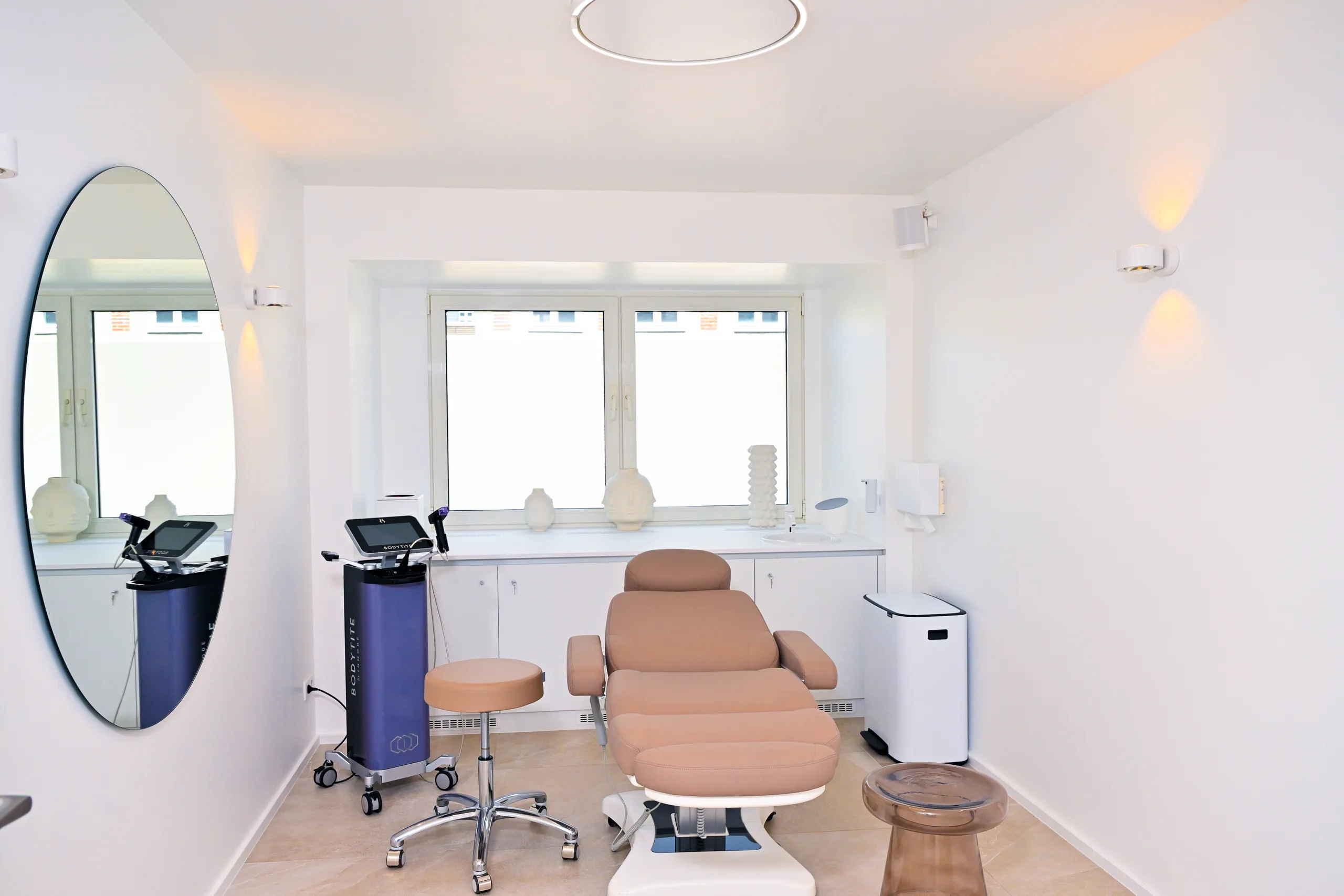 Bright treatment room at the artethic® practice in Düsseldorf with a treatment chair, a round mirror and a device on wheels.
