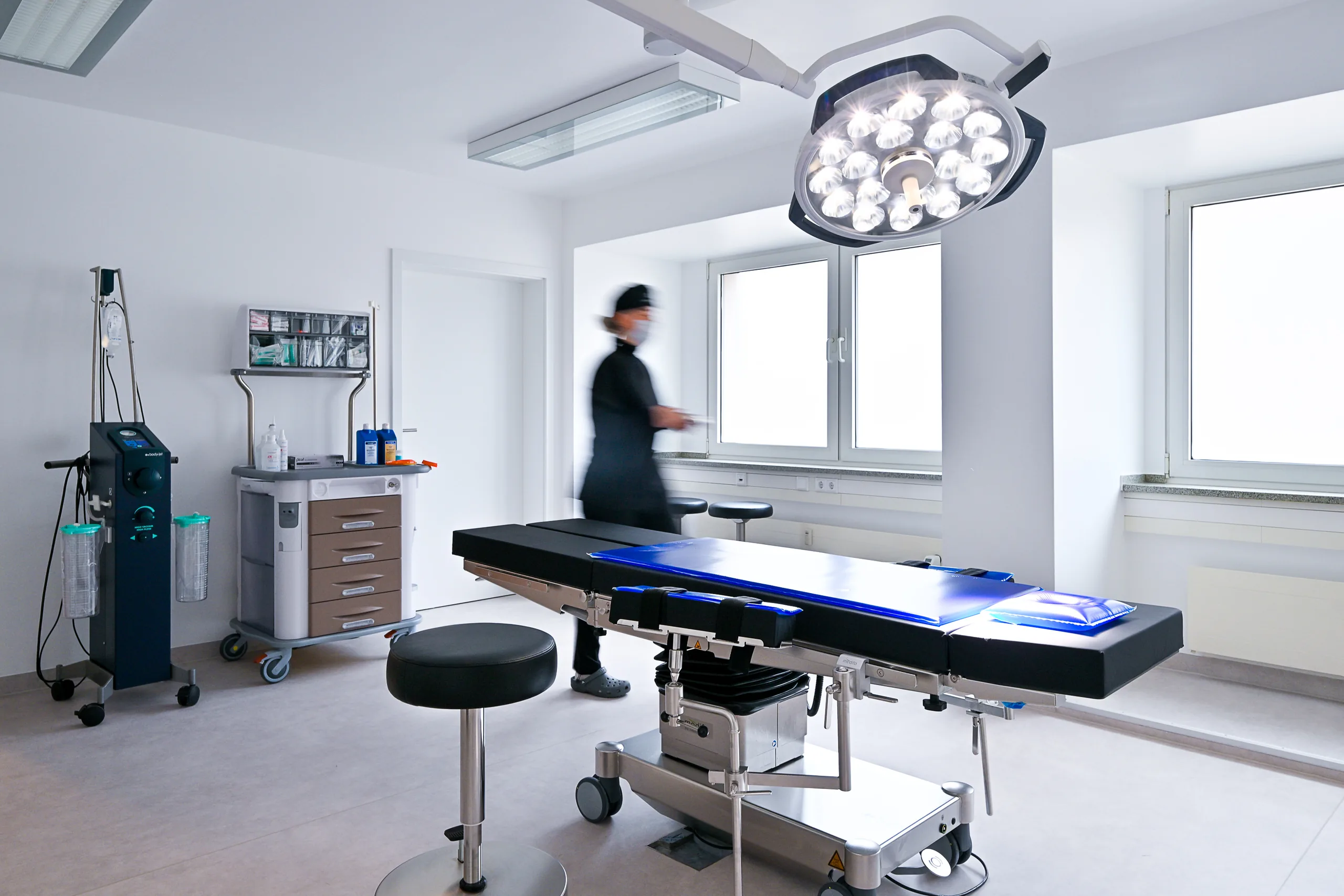 Procedure room at the artethic® practice in Düsseldorf with an operating table, a surgical light and a team member in motion.