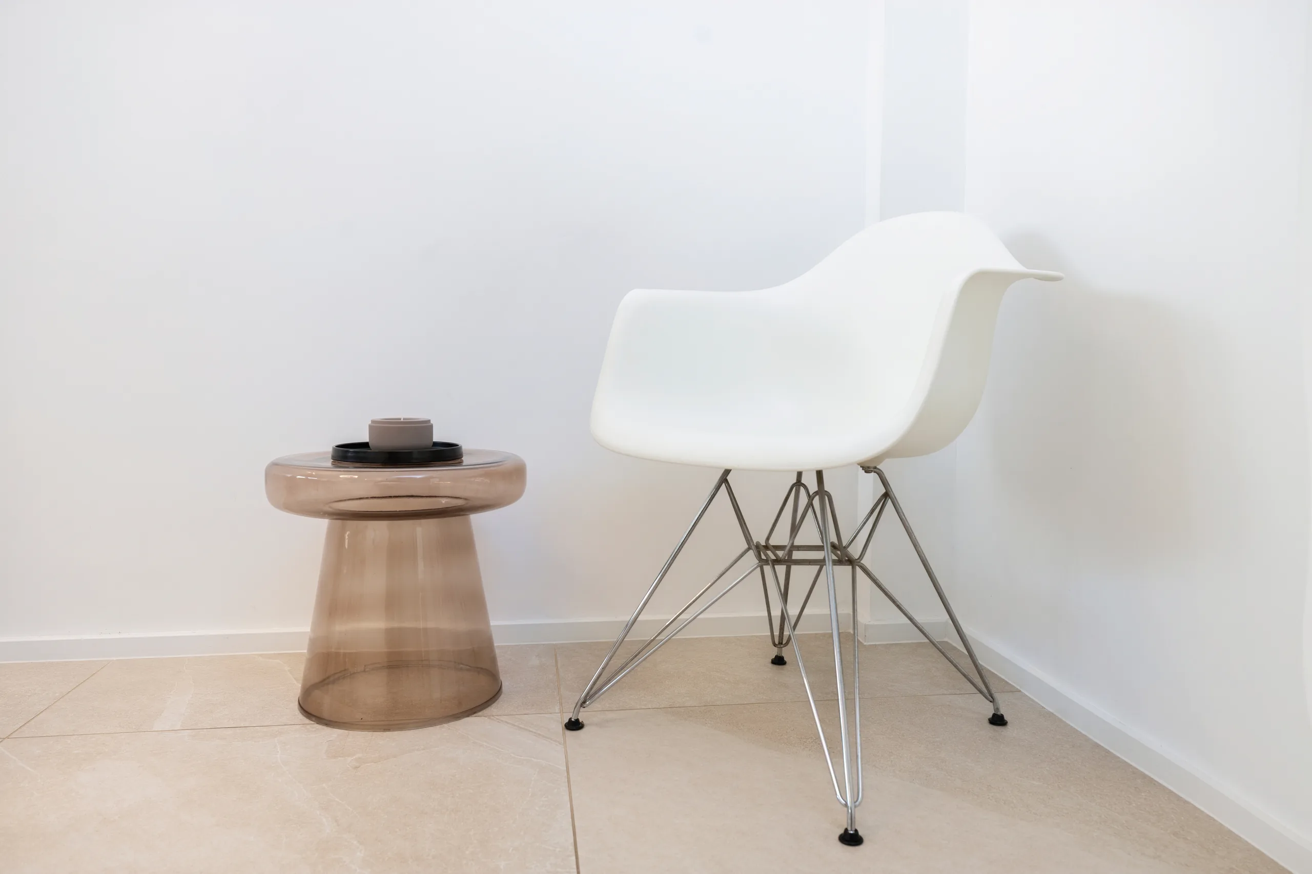 Seating area at the artethic® practice in Düsseldorf with a white shell chair and a tinted glass side table.