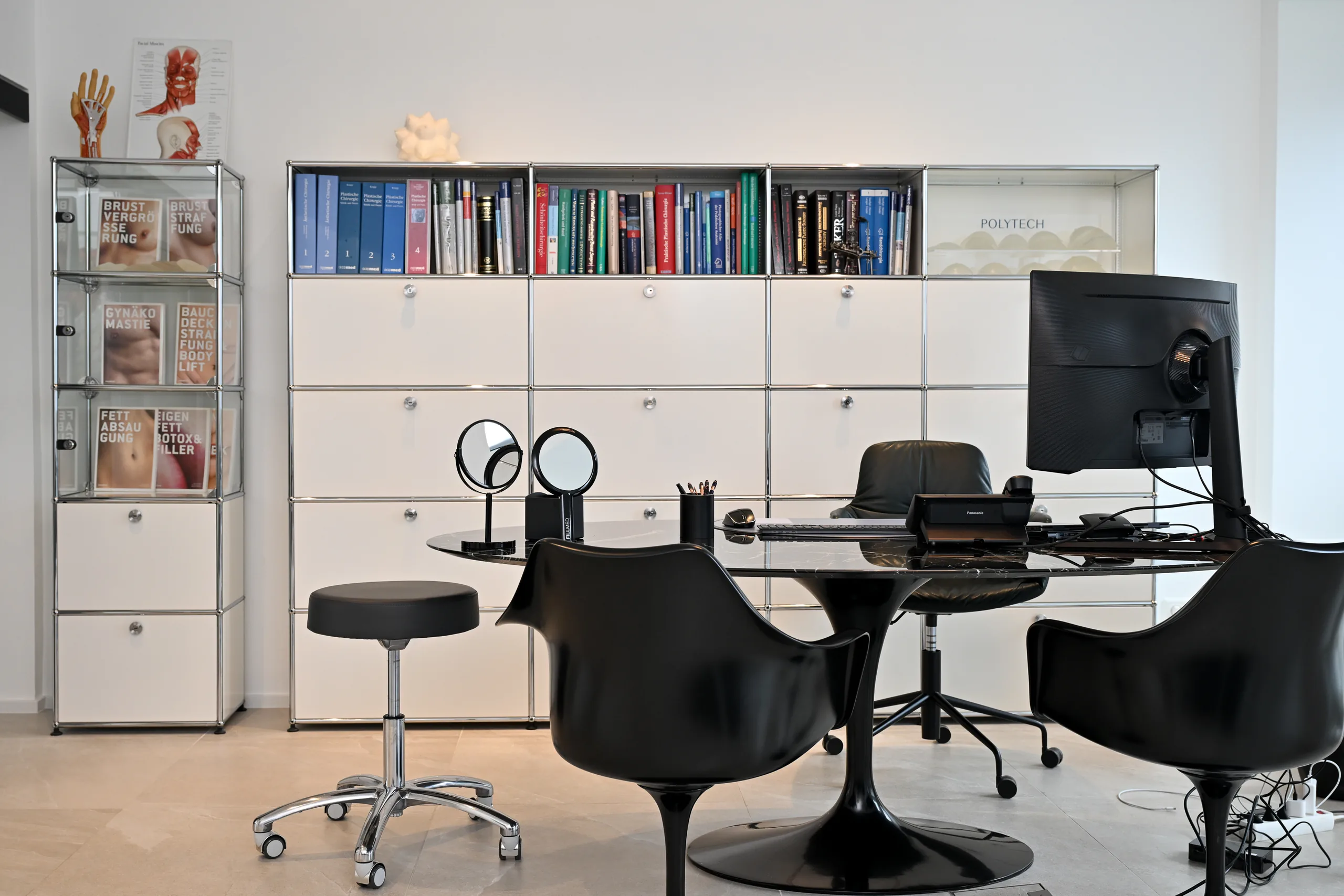 Sprechzimmer der Praxis artethic® in Düsseldorf mit Fachbüchern, anatomischen Handmodellen und schwarzem Tisch.