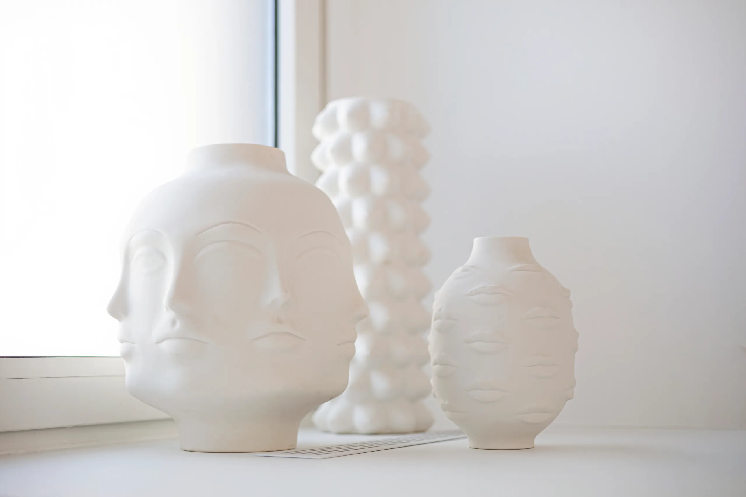 White vases with face motifs on a windowsill at the artethic® practice in Düsseldorf.