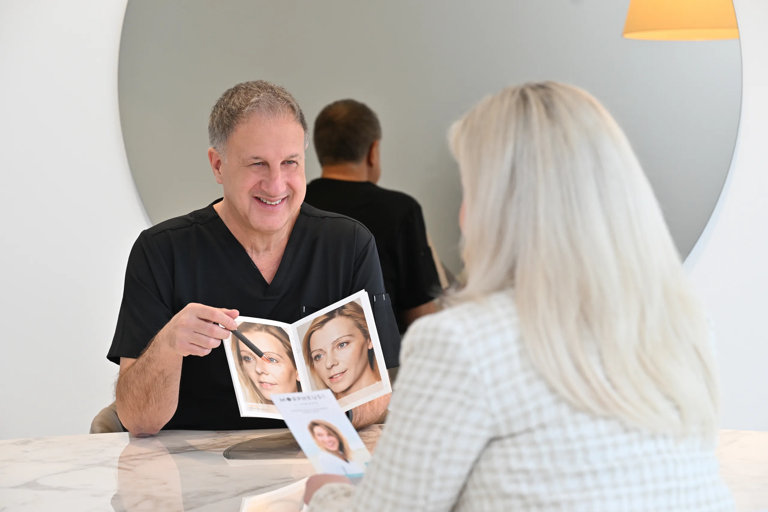 Dr. med. Karl Schuhmann showing a patient a brochure during a consultation at the artethic® practice in Düsseldorf.